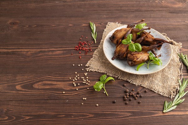 Smoked quails with herbs and spices on a ceramic plate with linen textile on a brown wooden