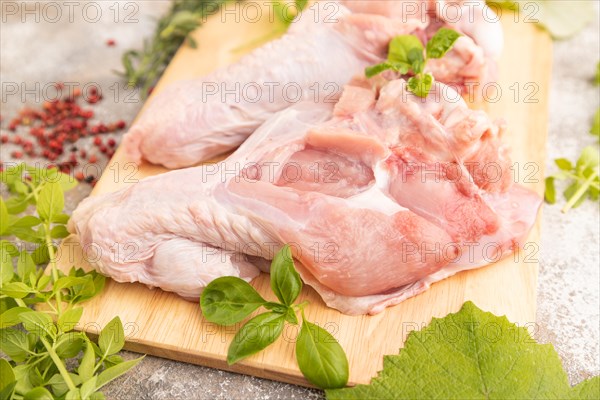 Raw turkey wing with herbs and spices on a wooden cutting board on a brown concrete background.