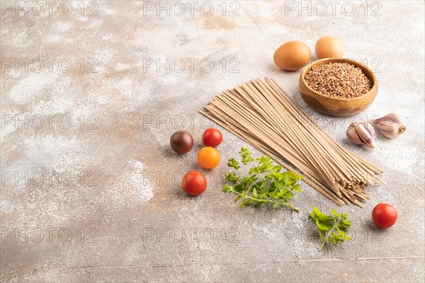 Japanese buckwheat soba noodles with tomato, eggs, spices, herbs on brown concrete background. Side