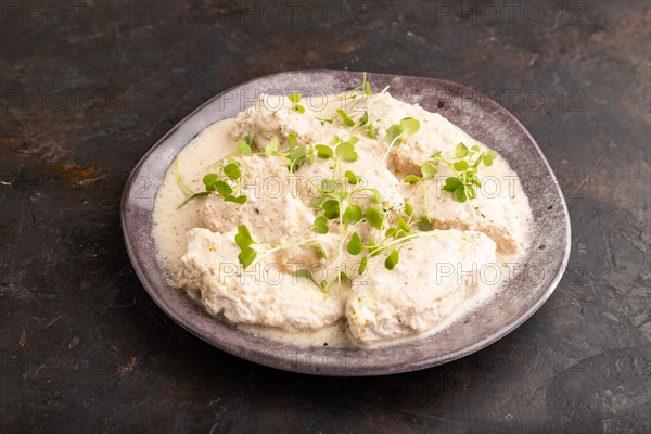 Stewed chicken fillets with coconut milk sauce and rucola microgreen on black concrete background.