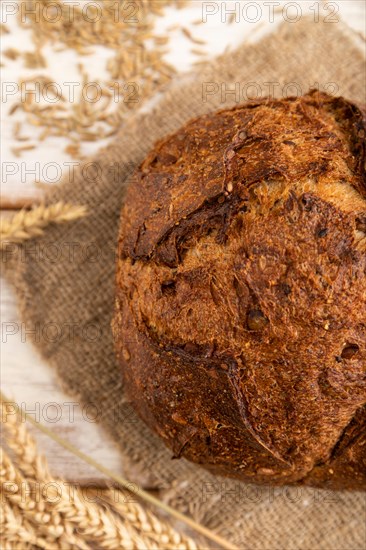 Fresh homemade golden grain bread with ears of wheat and rye on white wooden background and linen