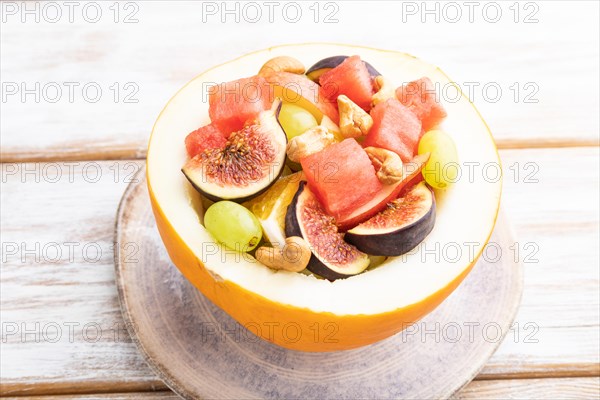 Vegetarian fruit salad of watermelon, grapes, figs, pear, orange, cashew on white wooden background