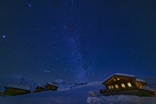 Mountain huts at night under a clear starry sky with illuminated windows in winter, Belalp, Naters,