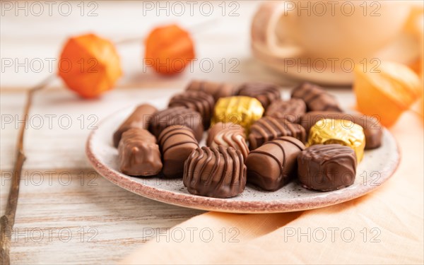 Chocolate candies with cup of coffee and physalis flowers on a white wooden background and orange