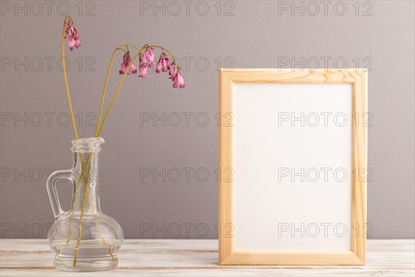 Wooden frame with pink dicentra, broken heart in glass on gray pastel background. side view, copy