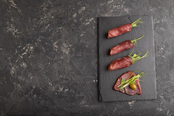 Slices of smoked salted meat with green pea microgreen on black concrete background. Top view, flat