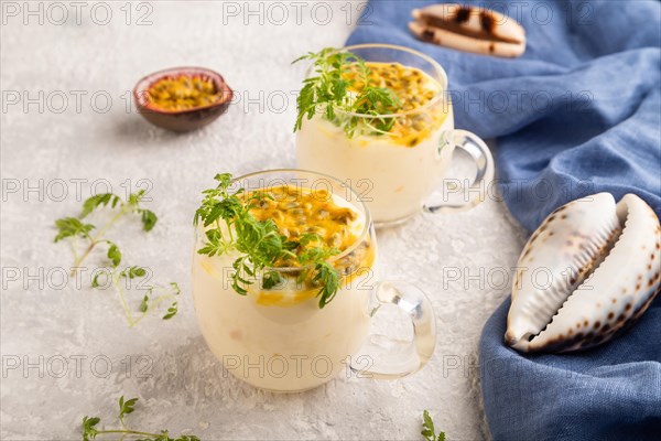 Yogurt with passionfruit and marigold microgreen in glass on gray concrete background with blue