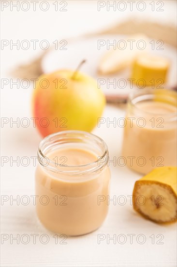 Baby puree with fruits mix, apple, banana infant formula in glass jar on white wooden background.