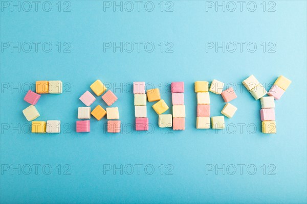 The inscription candy laid out with various fruit jelly chewing candies on blue pastel background.