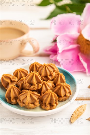Homemade soft caramel fudge candies on blue plate and cup of coffee on gray concrete background,