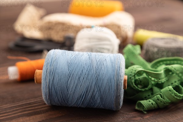 Sewing accessories: scissors, thread, thimbles, braid on brown wooden background. Side view, close