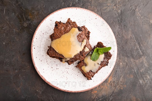 Chocolate brownie with caramel sauce with a cup of coffee on black concrete background. top view,