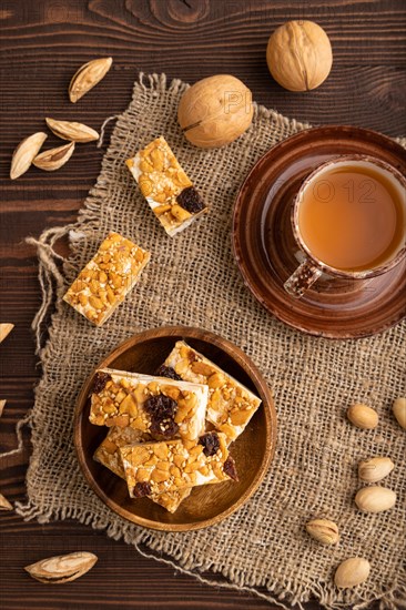 Traditional candy nougat with nuts and sesame with cup of green tea on brown wooden background and