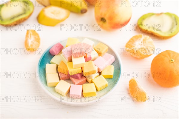 Various fruit jelly chewing candies on plate on white wooden background. apple, banana, tangerine,
