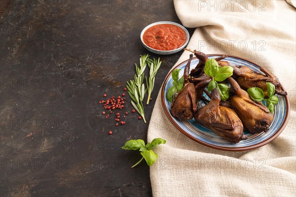 Smoked quail with herbs and spices on a ceramic plate with linen textile on a black concrete