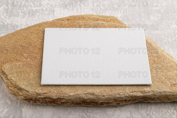 White paper business card, mockup with natural stone on gray concrete background. Blank, side view,