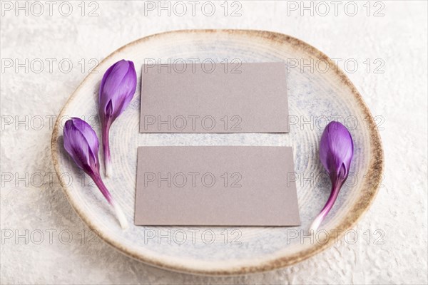 Gray paper invitation card, mockup with crocus flowers on ceramic plate and gray concrete