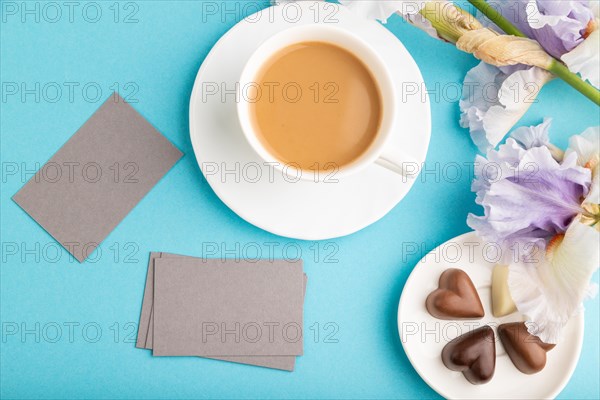 Gray business card with cup of cioffee, chocolate candies and iris flowers on blue pastel