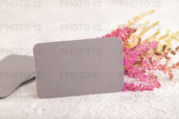 Gray paper business card mockup with purple astilbe flowers on gray concrete background. Blank,