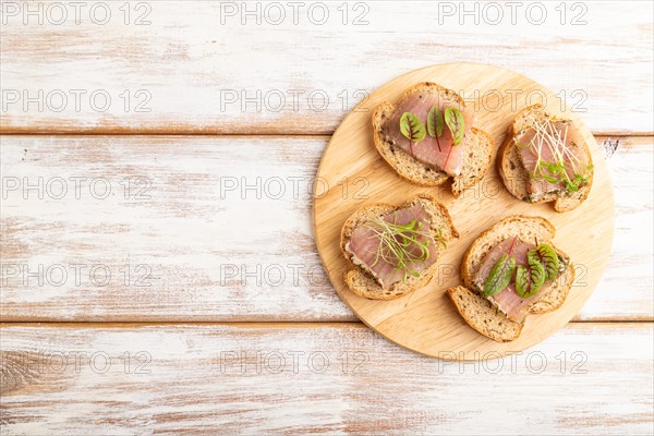Bread sandwiches with jerky salted meat, sorrel and cilantro microgreen on white wooden background.