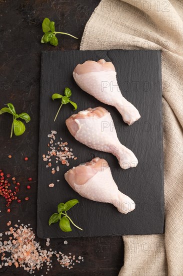 Raw chicken legs with herbs and spices on a black slate cutting board on a black concrete