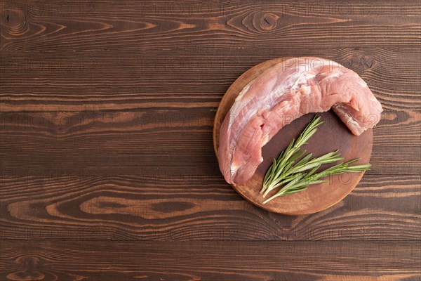 Raw pork with herbs and spices on a wooden cutting board on a brown wooden background. Top view,