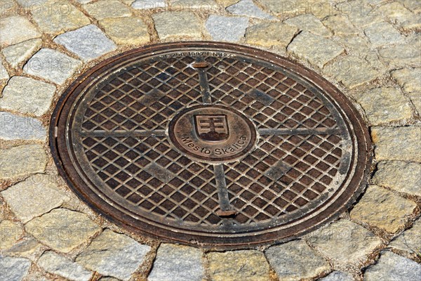 A metal manhole cover on a paved road surface, symmetrical and stable, manhole cover, Skalica,