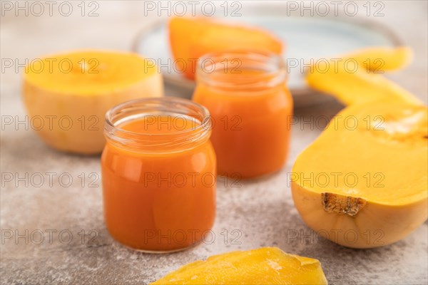 Baby puree with fruits mix, pumpkin, persimmon, mango infant formula in glass jar on brown concrete