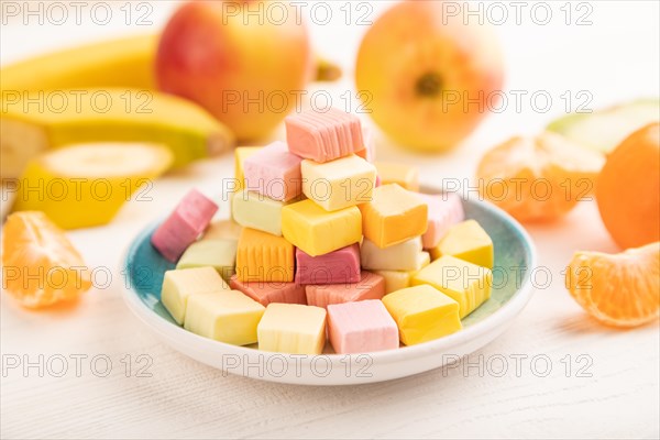 Various fruit jelly chewing candies on plate on white wooden background. apple, banana, tangerine,