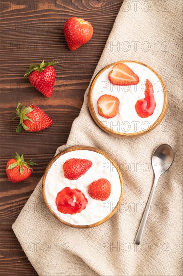 Grained cottage cheese with strawberry jam on brown wooden background and linen textile. top view,
