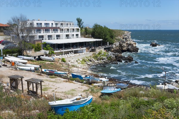 A hotel on the rocky coast with a view of the sea and several boats moored on the beach, harbour