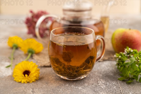 Red tea with herbs in glass teapot on brown concrete background and linen textile. Healthy drink
