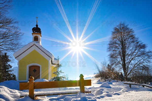 Backlit photograph of the snow-covered Maria Chapel on the hummocky meadows of Werdenfelser Land
