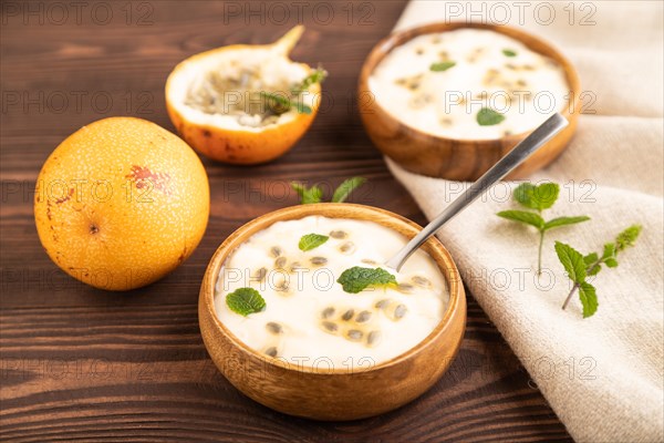 Yoghurt with granadilla and mint in wooden bowl on brown wooden background and linen textile. side