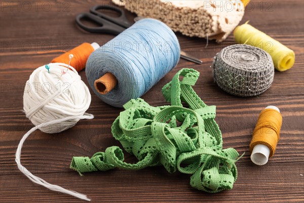 Sewing accessories: scissors, thread, thimbles, braid on brown wooden background. Side view, close