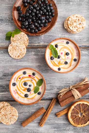 Yoghurt with bilberry and caramel in clay bowl on gray wooden background. top view, flat lay, close