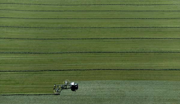 Farmer cutting grass to straight rows with tractor and large roundabout rake, drone shot, Upper