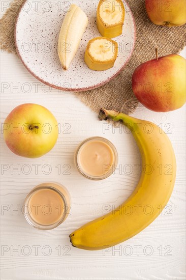 Baby puree with fruits mix, apple, banana infant formula in glass jar on white wooden background.