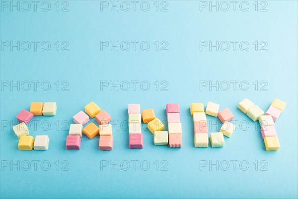 The inscription candy laid out with various fruit jelly chewing candies on blue pastel background.