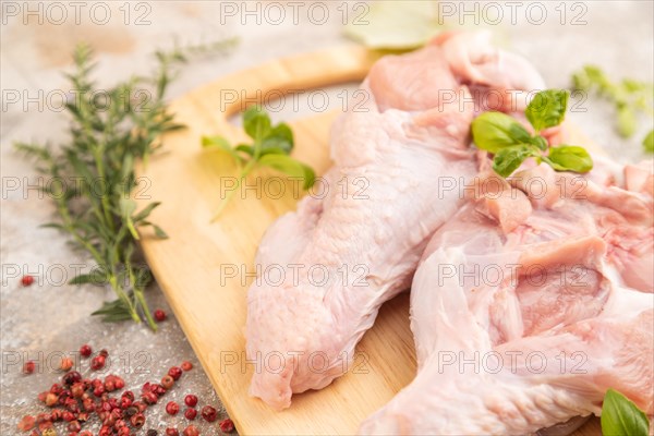 Raw turkey wing with herbs and spices on a wooden cutting board on a brown concrete background.
