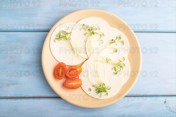 White cheese with tomatoes and cilantro microgreen on blue wooden background. top view, flat lay,