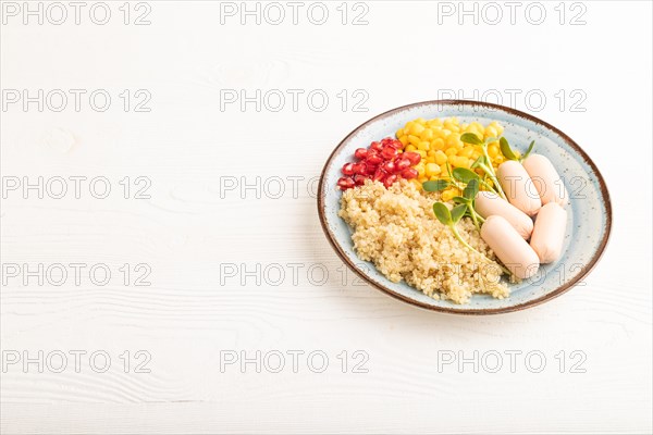 Mixed quinoa porridge, sweet corn, pomegranate seeds and small sausages on white wooden background.