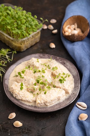 Stewed chicken fillets with coconut milk sauce and rucola microgreen on black concrete background