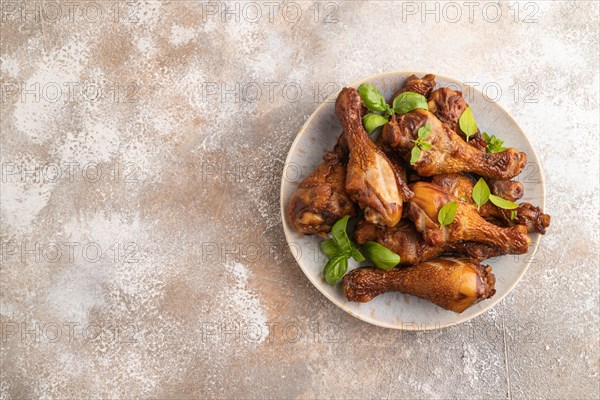 Smoked chicken legs with herbs and spices on a ceramic plate on a brown concrete background. Top