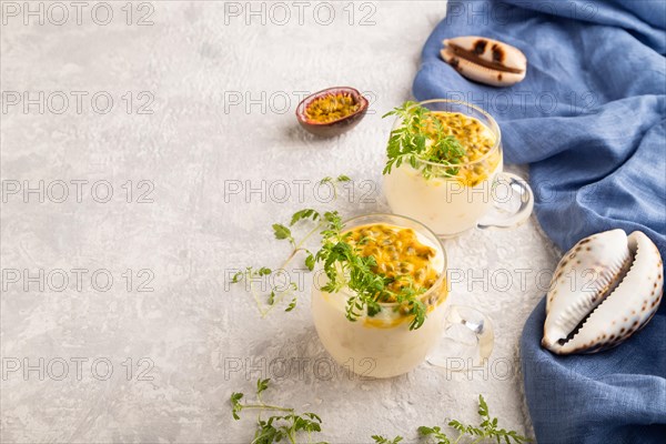 Yogurt with passionfruit and marigold microgreen in glass on gray concrete background with blue