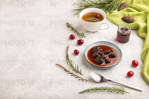 Pine cone jam with herbal tea on gray concrete background and green linen textile. Side view, copy