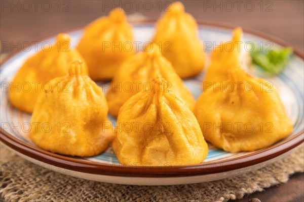 Fried manti dumplings with pepper, basil on brown wooden background and linen textile. Side view,