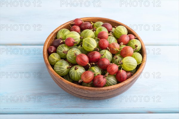 Fresh red and green gooseberry in wooden bowl on blue wooden background. side view, close up