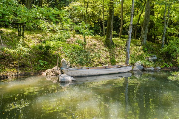 Wooden row boat in water at river bank in Shukkeien gardens in Hiroshima, Japan, Asia