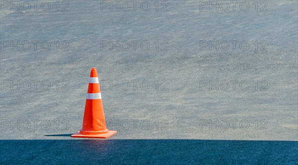 Orange traffic cone sitting in a pave parking lot on a sunny day with a shadow of a building in